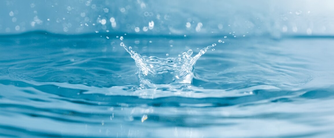 A close-up of a water drop hitting a clear blue surface and creating ripples.