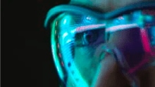 A person wearing safety goggles looks diagonally to the left and the image is enlarged focusing on the left eye.