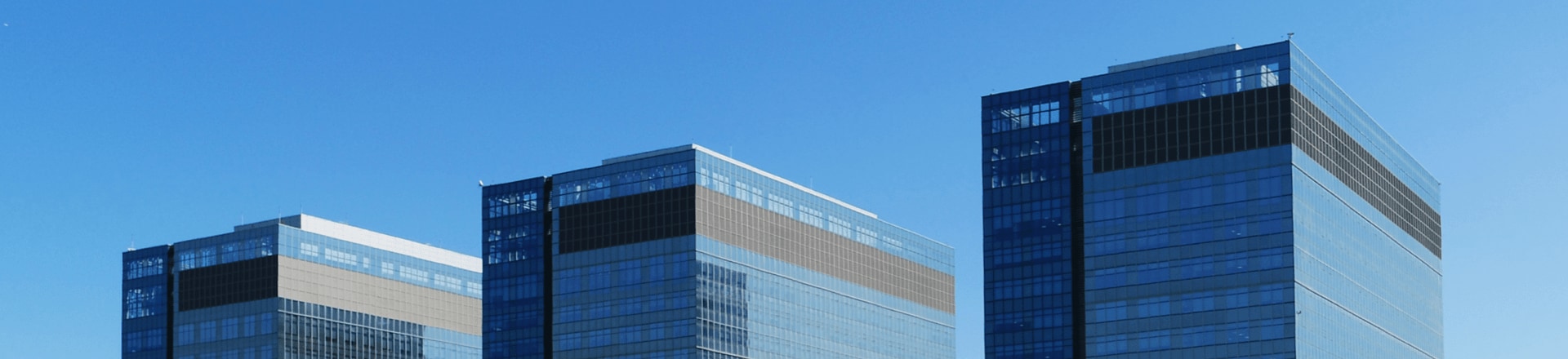Three modern high-rise buildings with glass facades sparkle under a blue sky.