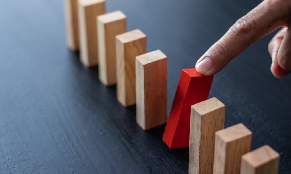 Close-up of finger knocking over a red wooden domino.