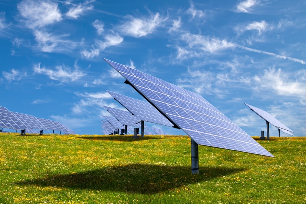 Individual solar panels seen placed across a grassy field under a cloudy sky.