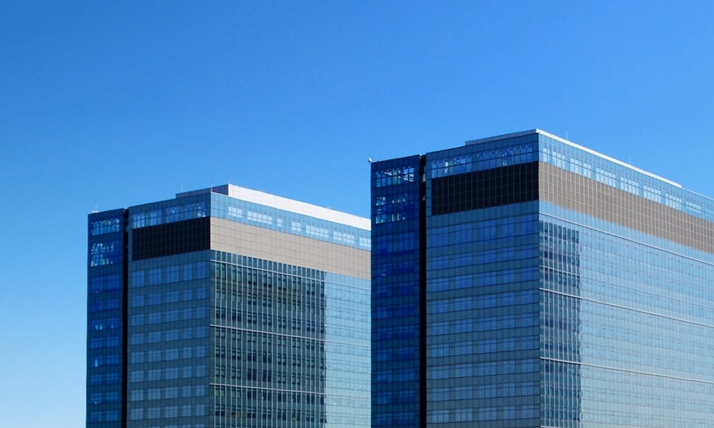 Two tall office buildings seen against a blue sky.