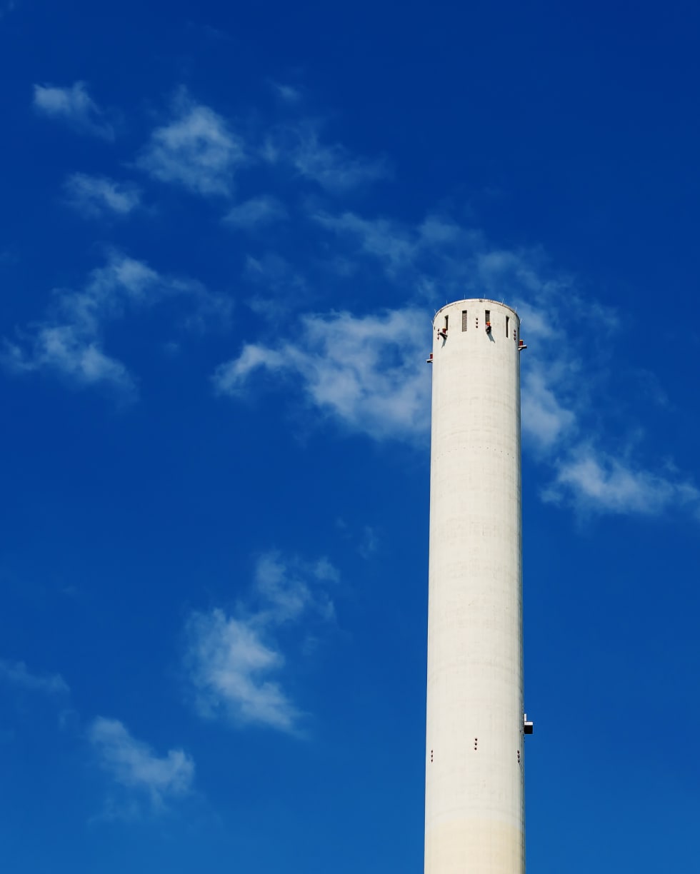 높고 원통형의 흰색 탑이 흩어진 구름이 있는 맑은 푸른 하늘을 배경으로 솟아 있습니다.