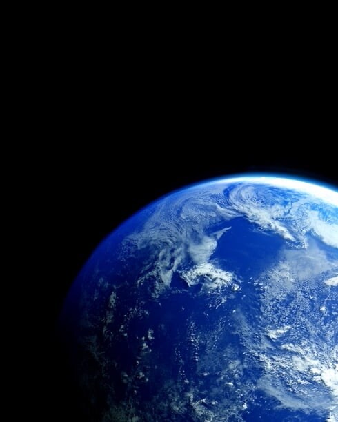The Earth glows blue in the vast, dark emptiness of space.